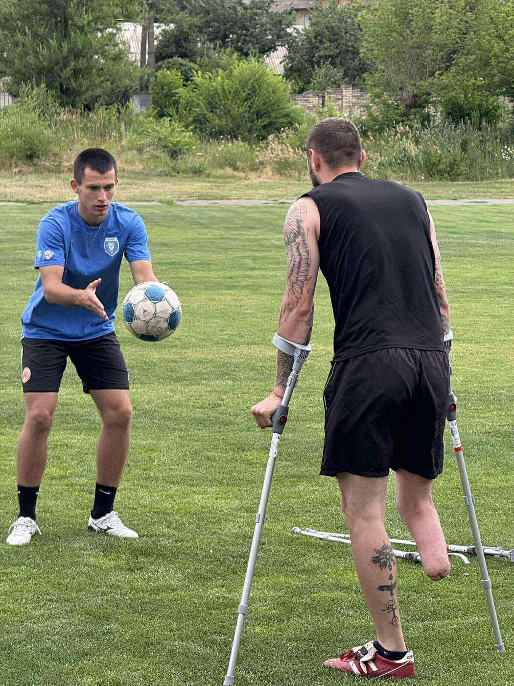 An amputee player on crutches trains with a coach on a soccer field
