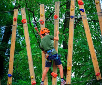 A camper in a helmet crosses a high ropes course at Camp Maximum